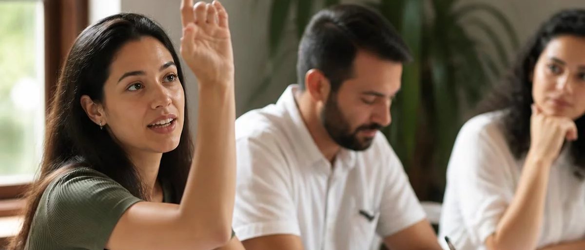 Participante com a mão erguida pedindo a vez, à mesa coberta de folhas escritas